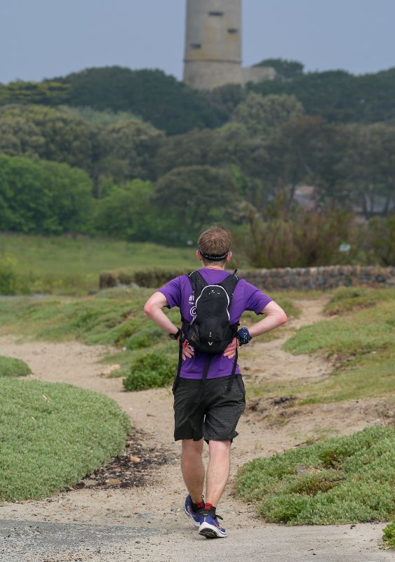 A male runner with hands on hip, walking towards a tower