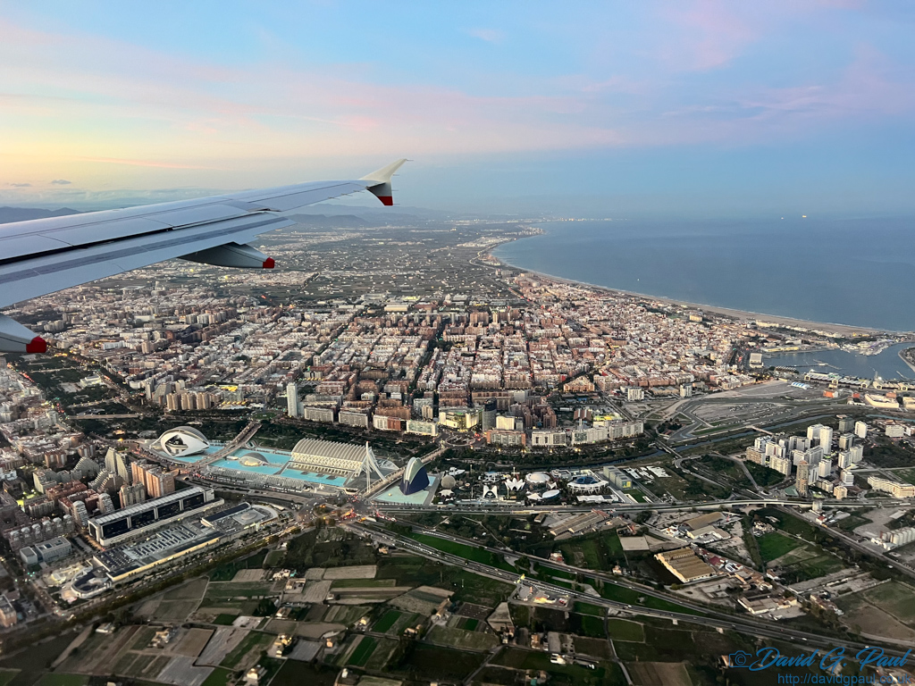 Beneath an aircraft wing you can see buildings and the sea below