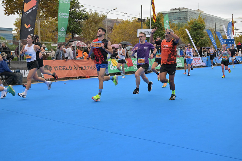 People running across a blue carpet towards an unseen finish line