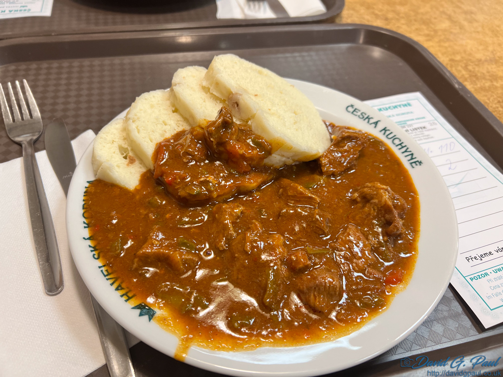 A plate filled to the rim with goulash and four bread dumplings