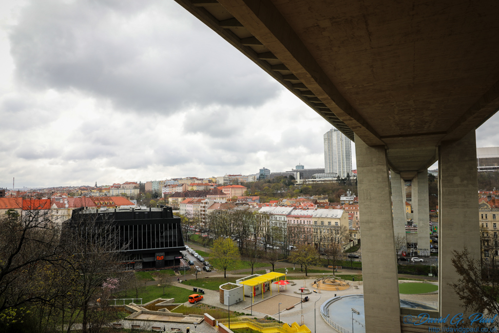 A very high bridge towers above a park and other buildings