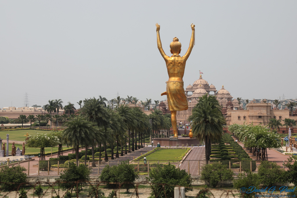 An avenue of trees with a tall golden statue in the middle with arms raised
