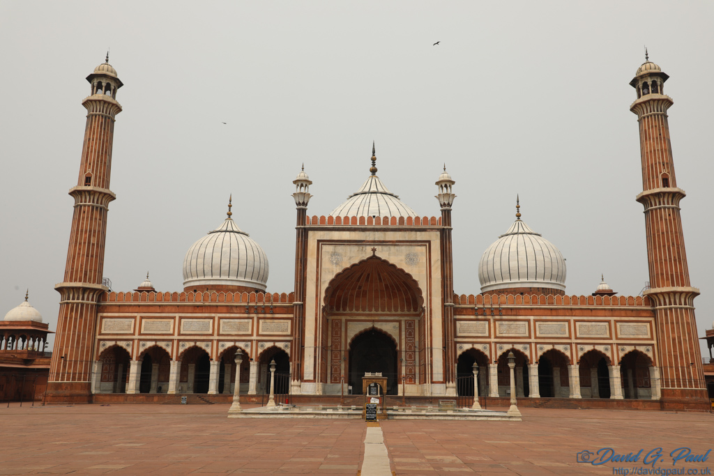 A red sandstone mosque with two minarets, and multiple white domes.