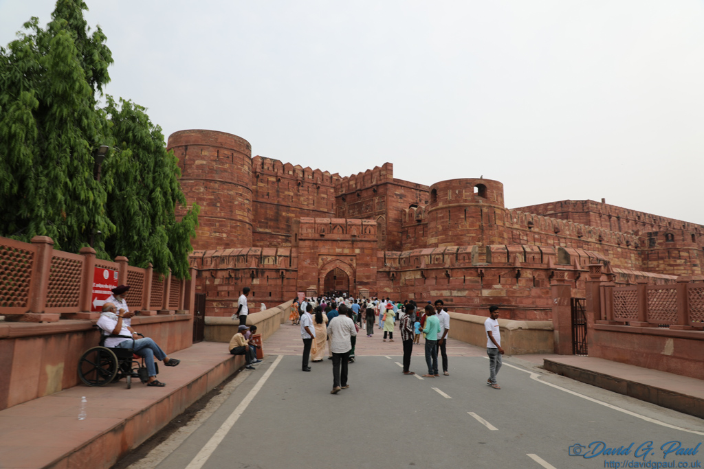 Many people standing outside red sandstone walls and gatehouse