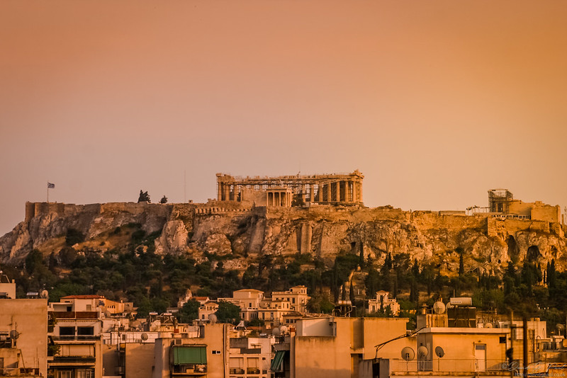 A red sky at night illuminates the Acropolis in Athens, with residential buildings in the foreground.