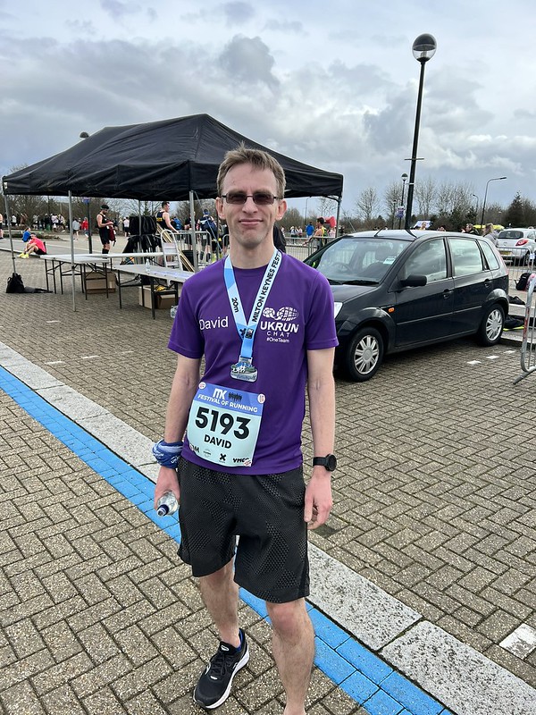 Male wearing purple t-shirt and blackc shorts with a medal around neck