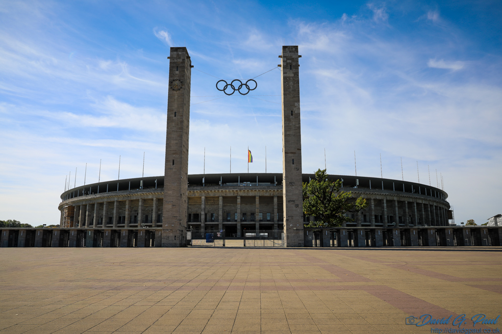 Olympic rings suspended between two pillars with a circular stadium behind