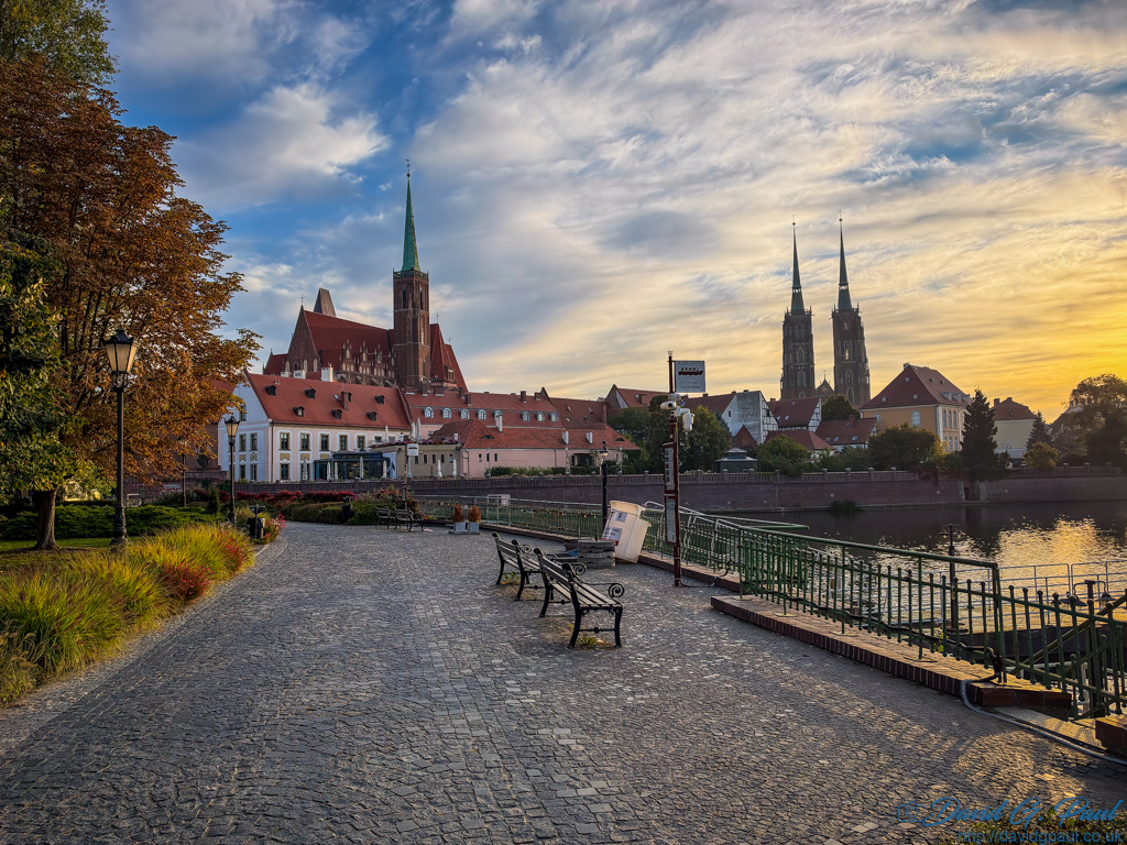 Cobbled street leading towards two churches. One has twin spires.