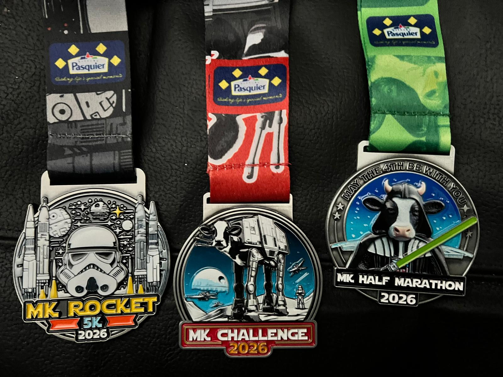 Three Star Wars themed running medals. MK Rocket 5K 2026 as a Stormtrooper helmet and two rockets either side. MK Challenge 2026 has an AT-AT with a cow head. MK Half Marathon 2026 is Darth Vader but with a cow's head.