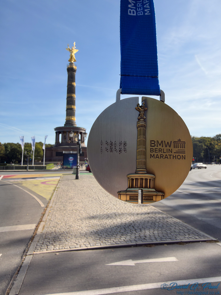 A Berlin Marathon medal is suspended in front of the Berlin Victory Column